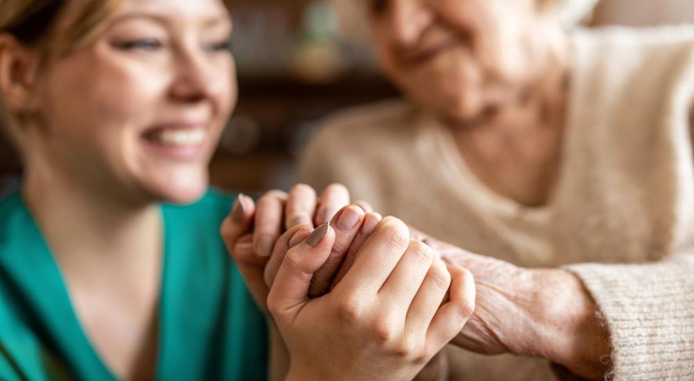 Senior en verzorgster houden elkaar vast